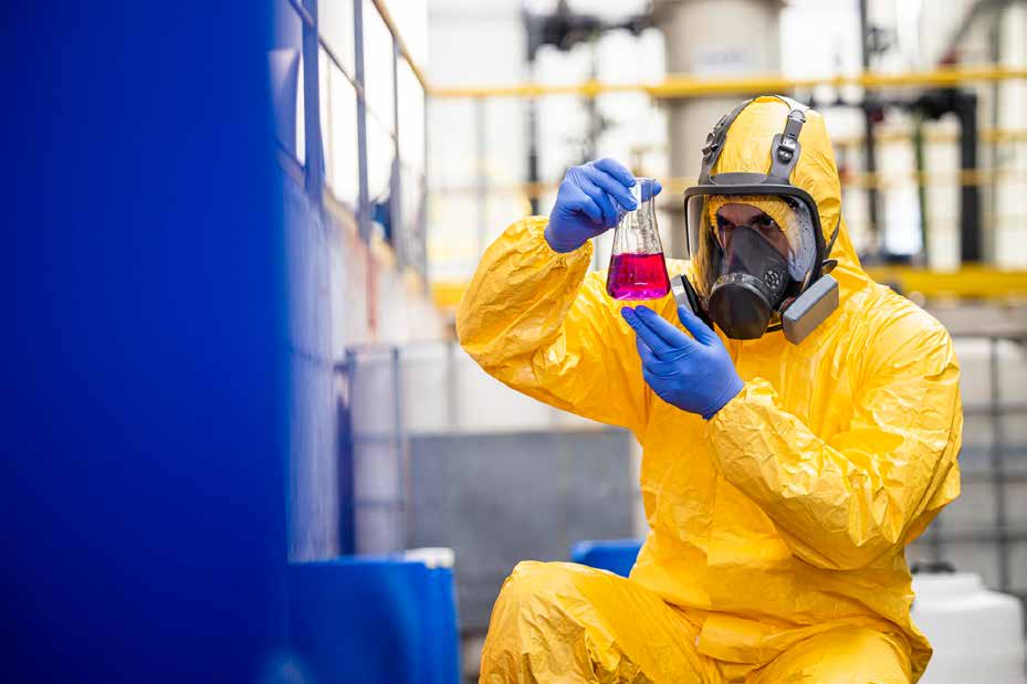 Industrial safety technician in hazmat suit inspecting chemical risk flask
